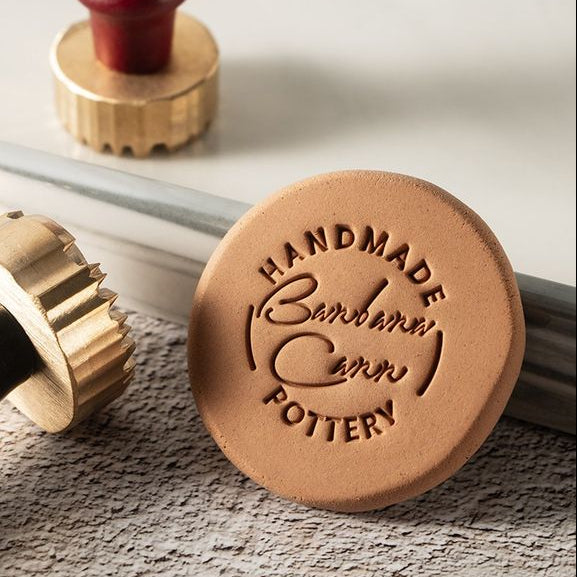 A personalised brass clay or ceramic stamp, showing the engraved text 'HANDMADE POTTERY'.